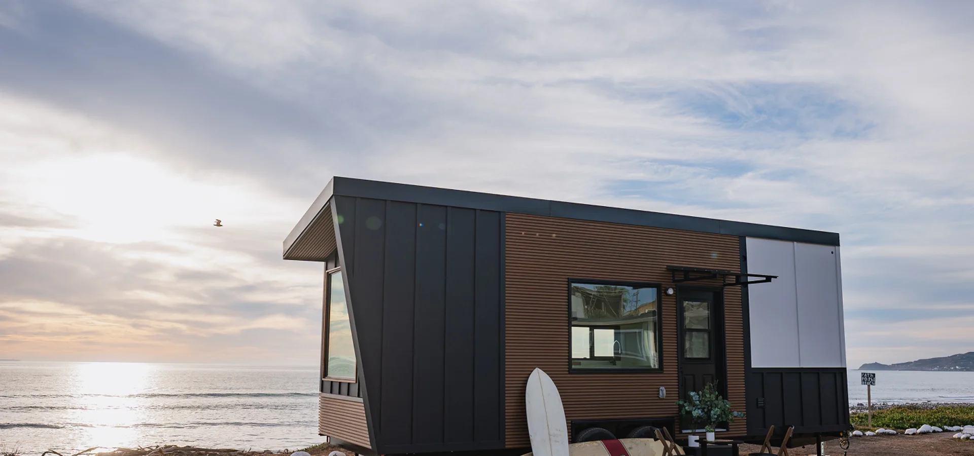 A Clever tiny home with timber siding and large windows beside the coast
